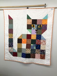 a quilt hanging on the wall with a cat made out of patchwork materials