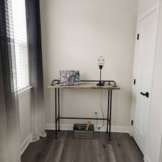 a room with white walls and wood flooring has a table on one side, lamp on the other