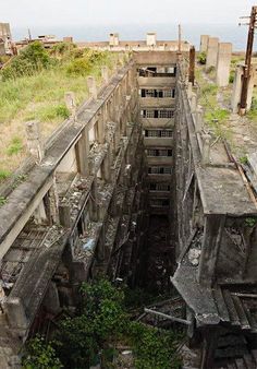 an old concrete building with lots of windows and doors in the middle of it, surrounded by overgrown vegetation