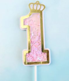 a cake shaped like the number one with pink and gold frosting on a stick