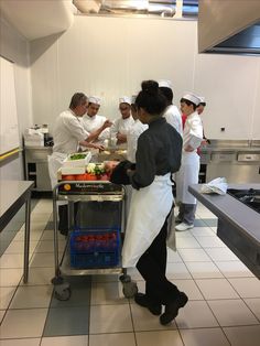 a group of people in a kitchen preparing food on top of a cart with utensils