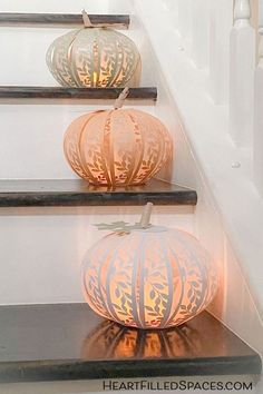 three pumpkins sitting on top of a set of stairs with paper lanterns attached to them