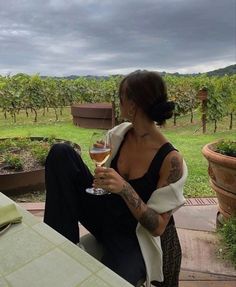 a woman holding a glass of wine on top of a wooden table in front of a field