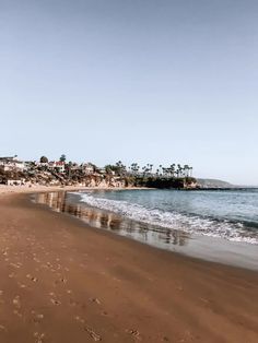 a sandy beach next to the ocean with houses on top of hill in the background