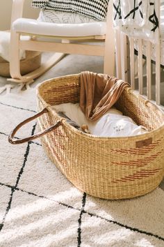 an empty basket sitting on the floor in front of a rocking chair with a blanket