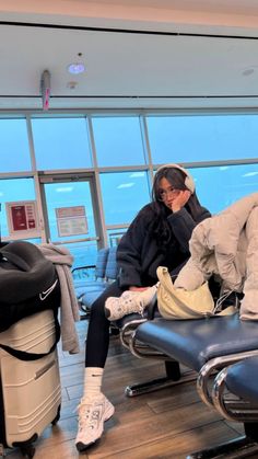 a woman sitting on top of an airport chair next to another person with headphones