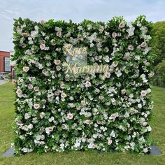 a large green wall with white and pink flowers on it's sides, surrounded by greenery