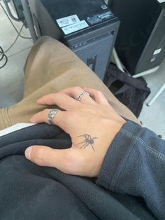 a woman's hand with a spider tattoo on her left wrist and two fingers