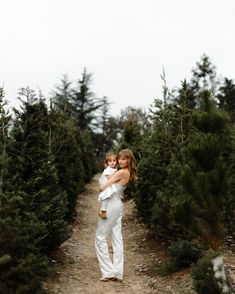 a woman holding a baby in her arms while walking down a dirt road surrounded by trees