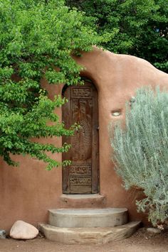 an adobe - style house with steps leading up to the front door and trees surrounding it