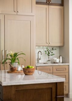 a kitchen with wooden cabinets and white marble counter tops, two bowls filled with fruit on the island