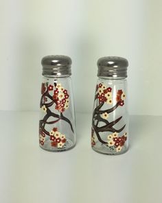 two glass salt and pepper shakers with flowers painted on the side, sitting next to each other