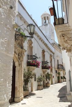 an alley way with white buildings and flowers on the balconies