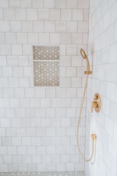 a white tiled shower with gold fixtures and hand held shower head on the wall next to it