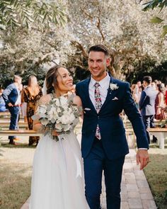 a bride and groom walking down the aisle at their outdoor wedding ceremony with guests in the background