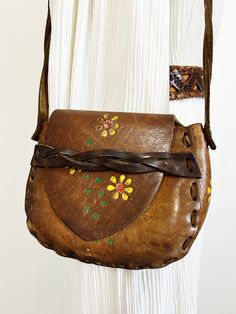 |d e s c r i p t i o n| *circa 1970s *beautiful hippie leather purse from the 70s, came from original owner  *hand tooled design with painted yellow daisies  *saddle flap in front with strap  *a good length arm strap, could be snug cross body purse  *clean inside, well taken care of!  *authentic boho/hippie shoulder bag  |i n f o| tag: none  condition: very good! A few stretches on outside of leather.  |m e a s u r e m e n t s| total length with strap: 22" length of purse: 8.5" height of purse: Hippie Brown Leather Bag, Brown Leather Hippie Bag, Mid-century Brown Leather Bags, Hippie Leather Shoulder Bag For Everyday, Vintage Hand-tooled Festival Shoulder Bag, Mid-century Leather Shoulder Bag For Daily Use, Vintage Satchel Shoulder Bag For Festival, Vintage Brown Bohemian Leather Bag, Purse Cleaning