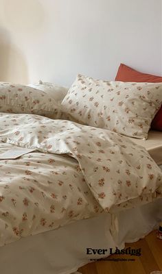 an unmade bed with white sheets and floral print on it, in a bedroom