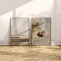 two framed paintings on the wall in an empty room with wood flooring and white walls