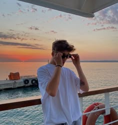 a man talking on a cell phone while standing next to a boat in the ocean