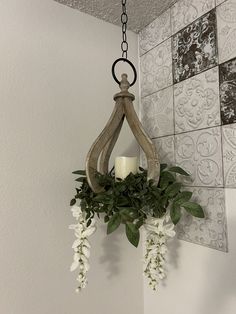 a candle hanging from the ceiling with flowers and greenery on it's side