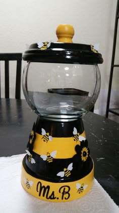 a yellow and black glass jar with bees on it sitting on top of a table