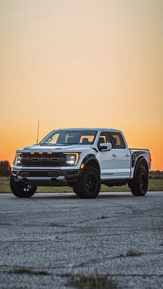 a white truck parked on top of an airport tarmac at sunset with the sun setting in the background