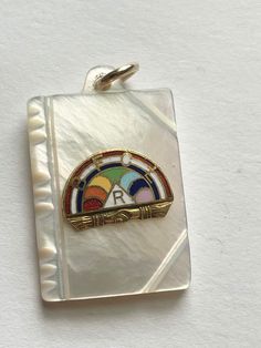 This is a beautiful vintage mother of pearl enamel and 10 karat gold, rainbow girls pendant It has a mother of pearl base with a beautiful colored enamel rainbow with the letters BFCL as well as the letter R .  Both the rainbow section as well as the jump ring test positive as 10 K gold The pendant is in the shape of a book The piece measures 7/8" x 5/8 This item is an excellent preowned vintage condition with normal wear for age. There are no chips to the mother of pearl. Retro Rainbow Jewelry For Gifts, Art Deco Multicolor Jewelry For Gift, Rainbow Retro Jewelry For Gift, Retro Rainbow Jewelry Gift, Retro Rainbow Colored Jewelry Gift, Multicolor Art Deco Jewelry For Gift, Multicolor Art Deco Jewelry Gift, Mother Of Pearl Pendant, Vintage Rainbow