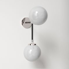 two white balls are attached to the wall by a metal rod and one light is turned on