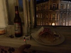 a person holding a wine glass near a plate with food on it and a bottle in the window sill