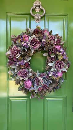 a green door with a wreath hanging on it's side and purple flowers in the middle