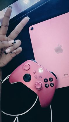 a pink controller sitting next to an apple ipad and a woman's hand holding the peace sign