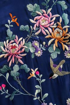 an embroidered fabric with flowers and birds on it, including one bird flying in the air