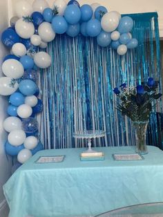 blue and white balloons are hanging over a table with a vase full of flowers on it