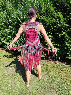 a woman in a pink and purple dress walking through the grass with her hand on her hip