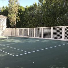 a tennis court with a white fence and trees in the background