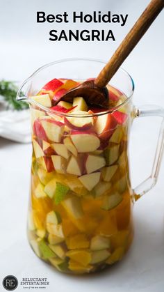 a glass pitcher filled with sliced apples on top of a white table next to a wooden spoon