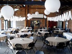 tables and chairs are set up for an event with white paper lanterns hanging from the ceiling