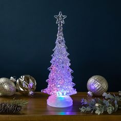 a lighted christmas tree sitting on top of a wooden table next to silver balls and pine cones