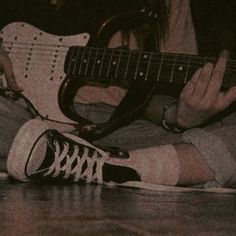 a man sitting on the floor with his feet up and holding an electric guitar in front of him