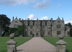 an old mansion with stone pillars and gated walkway leading to the front door, surrounded by lush green grass