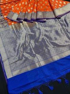 Traditional Orange Banarasi Silk Saree with Purple Borders and Blue Pallu with matching blouse piece. Saree is super soft!! Please note - Borders are wide. Approx. 7 1/2 inches Small Buttis all over the body of the Saree with Grand Pallu and Tassels Item : SareeColor : Orange/ Purple/Blue Base Fabric : Banarasi Silk SareeBlouse piece : Comes with Blouse pieceBlouse material : Banarasi Silk SareeFall & Edging done (Yes/No) : YesDisclaimer -:- Color variation is possible due to various reasons lik Orange Banarasi Silk Set With Dupatta, Fusion Style Semi-stitched Dupatta For Navratri, Fusion Multicolor Traditional Wear With Zari Work, Designer Fusion Dupatta For Festivals, Festive Fusion Blouse Piece With Pallu, Fusion Style Designer Wear Dupatta For Festivals, Fusion Style Multicolor Dupatta With Pallu, Multicolor Fusion Dupatta With Pallu, Multicolor Fusion Style Dupatta With Pallu