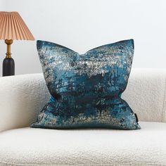 a blue pillow sitting on top of a white couch next to a light colored lamp