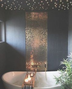 a bathtub with candles in the middle and lights on the wall above it, next to a potted plant