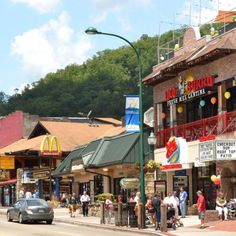 people are walking on the sidewalk in front of shops and restaurants near a street light