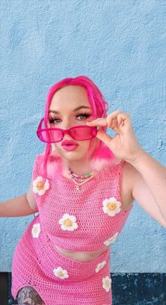 a woman with pink hair and glasses is posing for the camera in front of a blue wall