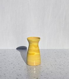 a yellow vase sitting on top of a table next to a shadow cast by the wall