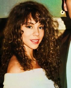 a close up of a person wearing a white dress and smiling at the camera with long curly hair