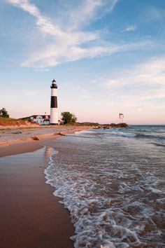 the beach has waves coming in to shore and a light house on the other side