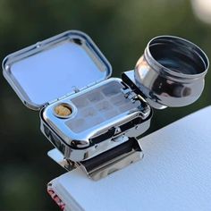 an open silver camera lens sitting on top of a white box with its lid opened