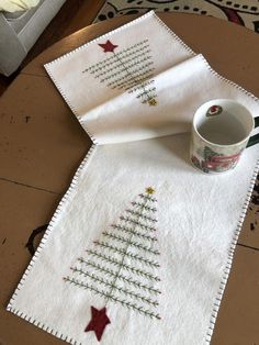 two christmas tree napkins on top of a wooden table with a coffee cup in the middle